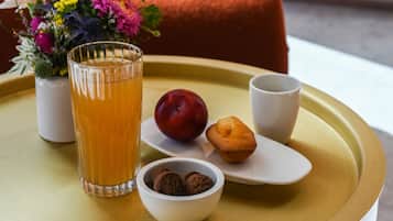 A tray with a glass of orange juice, a plum, a muffin, and a bowl of cookies on a round table.