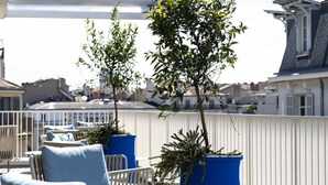 Un balcón con mobiliario de mimbre, plantas en macetas y vistas de la ciudad.