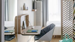 Una habitación de hotel moderna con cama, escritorio, silla, televisor y armario.