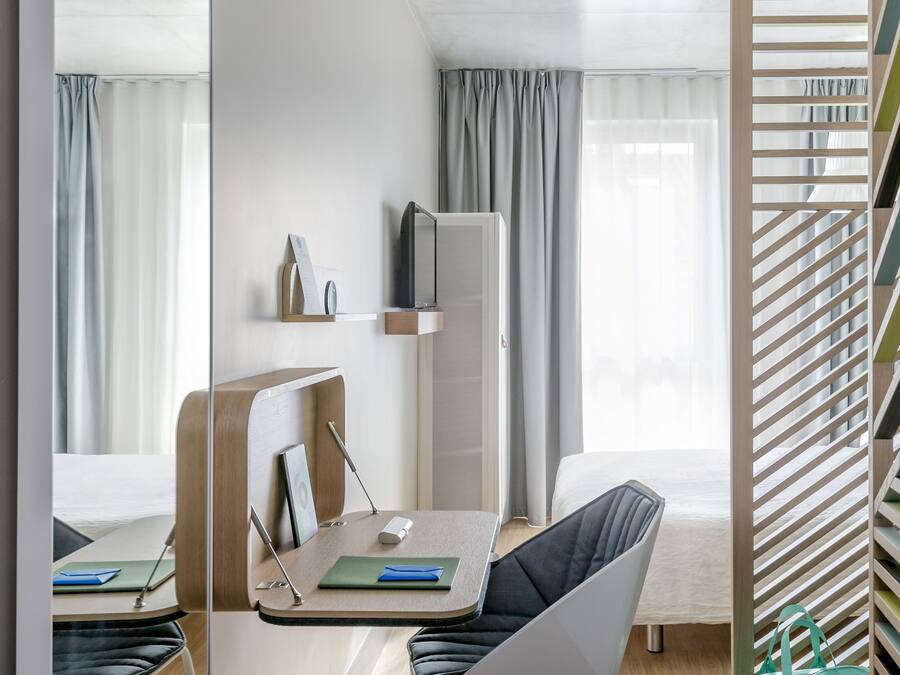Ein modernes Hotelzimmer mit Bett, Schreibtisch mit Stuhl, Fernseher und Kleiderschrank.