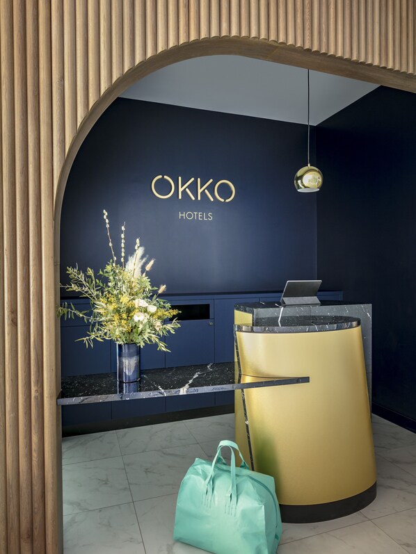 A reception area with a dark blue wall, a wooden slat arch, and a reception desk with a laptop.