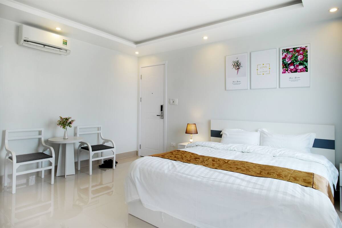 A hotel room with a bed, bedside table, lamp, two chairs, and a small table with a vase of flowers.