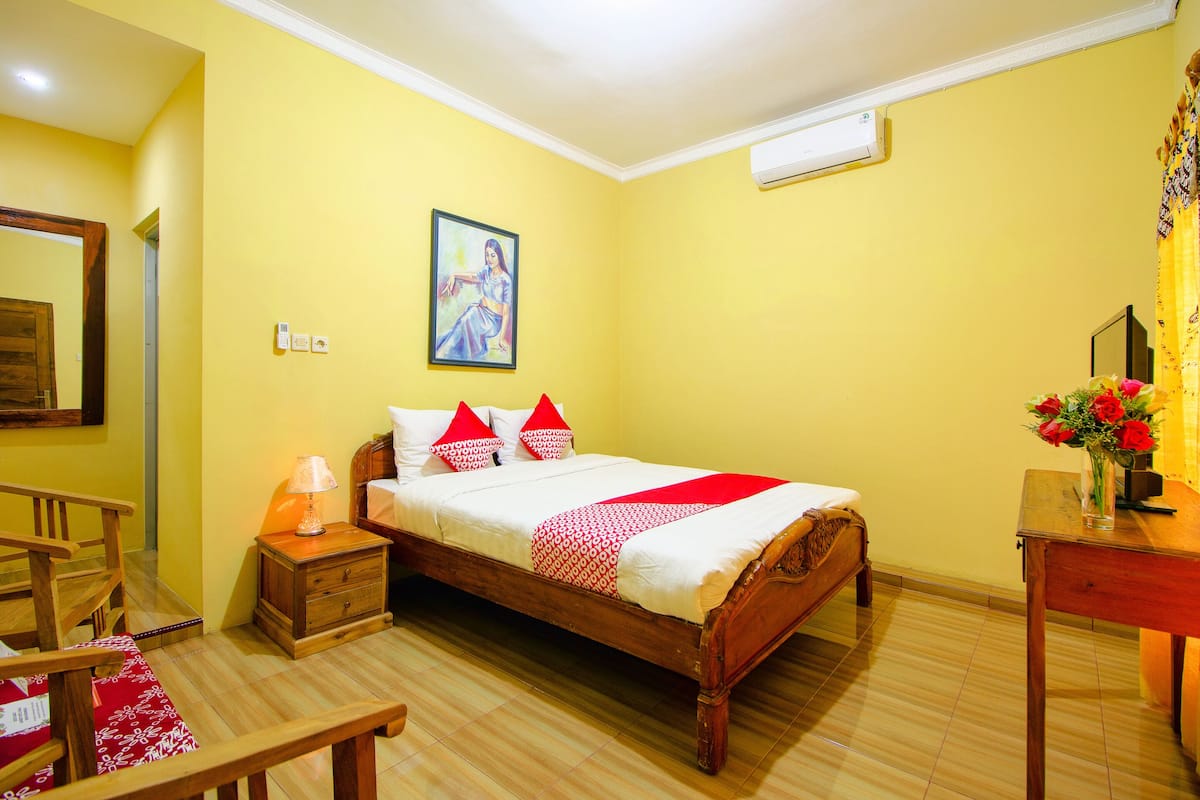 Ein Hotelzimmer mit einem Holzbett, einem Nachttisch mit Lampe, einem Schreibtisch mit Blumenvase und einem Bild an der Wand.