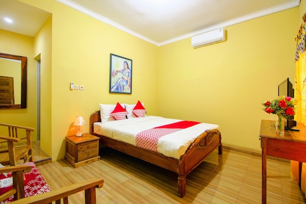 A hotel room with a wooden bed, a nightstand with a lamp, a desk with a vase of flowers, and a painting on the wall. - Hotel O Opak Village Bed & Breakfast (Jetis)