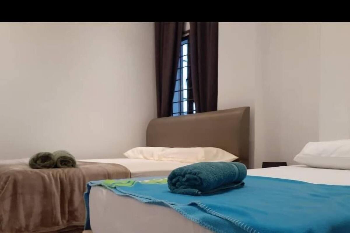 Habitación de hotel con dos camas, cada una con un edredón de diferente color, y una ventana con cortinas.
