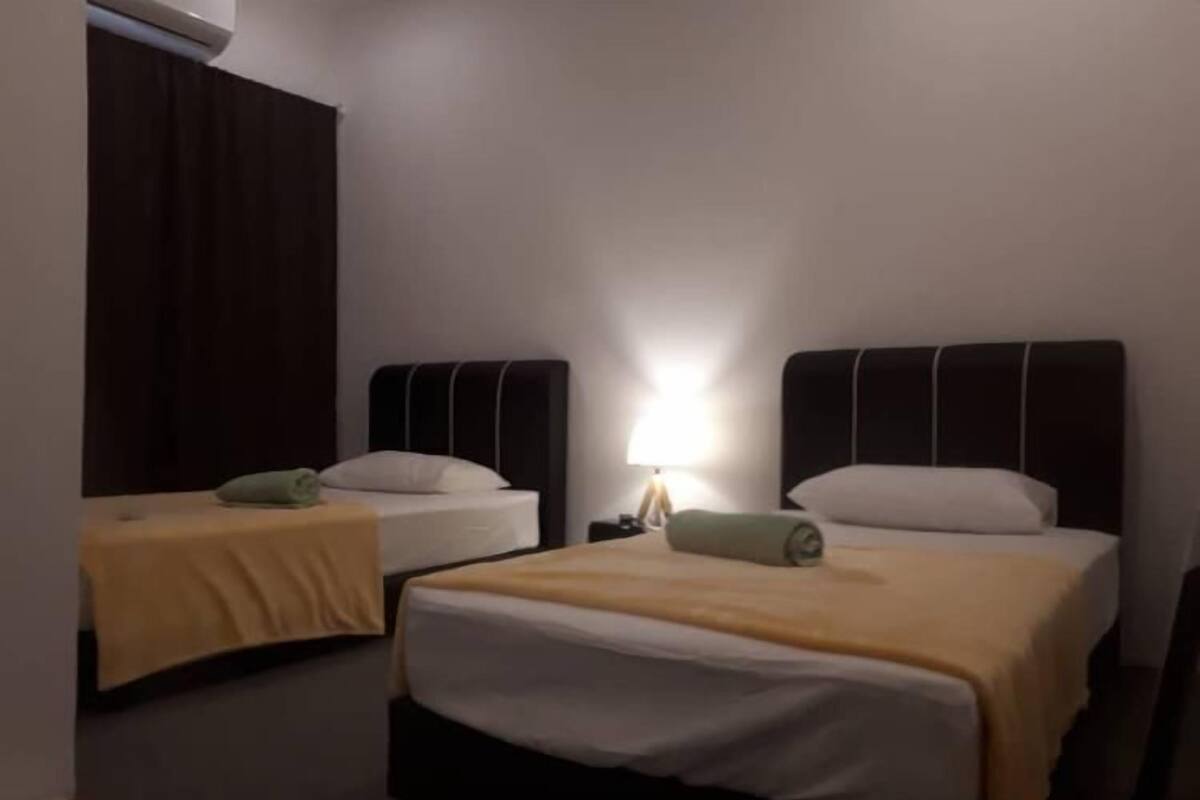Una habitación de hotel con dos camas individuales, una mesita de noche con lámpara y una cortina oscura.