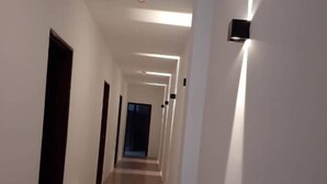 A long, narrow hallway with white walls and a tiled floor. There are doors on both sides and a light fixture on the right wall. - Comfortable Stay (George Town)