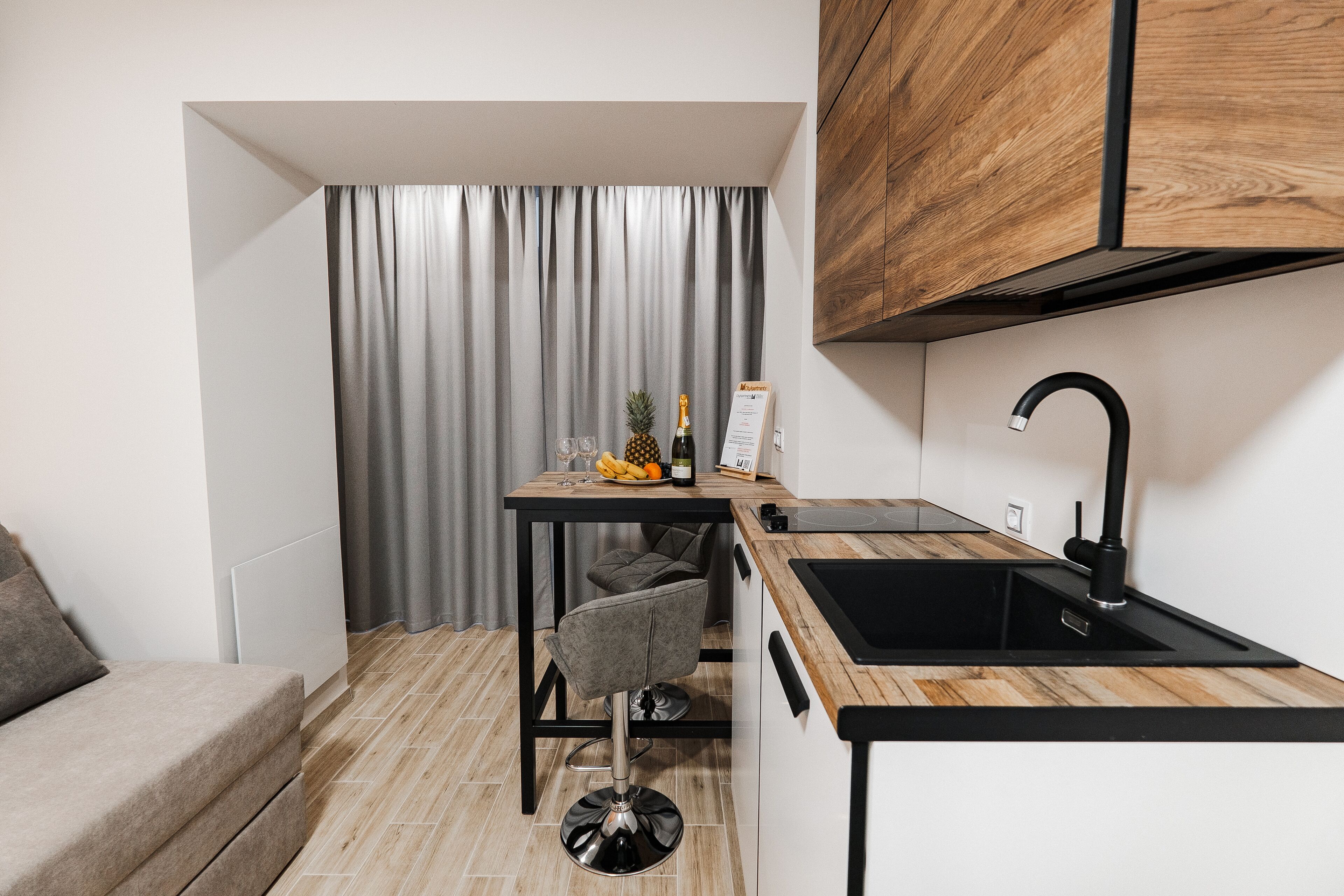 A compact kitchen with a wooden countertop, a black sink, and a small dining area with a chair.