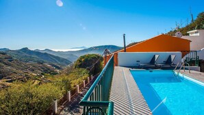 A pool with a view of mountains, a wooden deck, and two lounge chairs. - El Mimo rural cave house (Artenara)