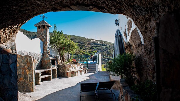A stone pathway leading to a pool area with a view of a hill and a church. - El Mimo rural cave house (Artenara)