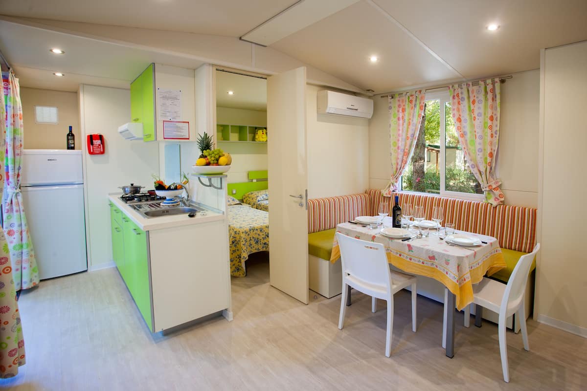 A compact kitchen with a refrigerator, stove, and sink. There is a dining area with a table set for two, chairs, and a bench.