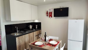 Una cocina compacta con encimera negra, armarios de madera, refrigerador blanco y una mesa de comedor para dos personas, con individuales rojos.