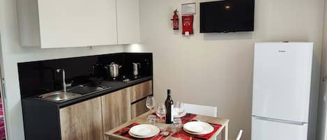 A compact kitchen with a black countertop, wooden cabinets, a white refrigerator, and a dining table set for two with red placemats.