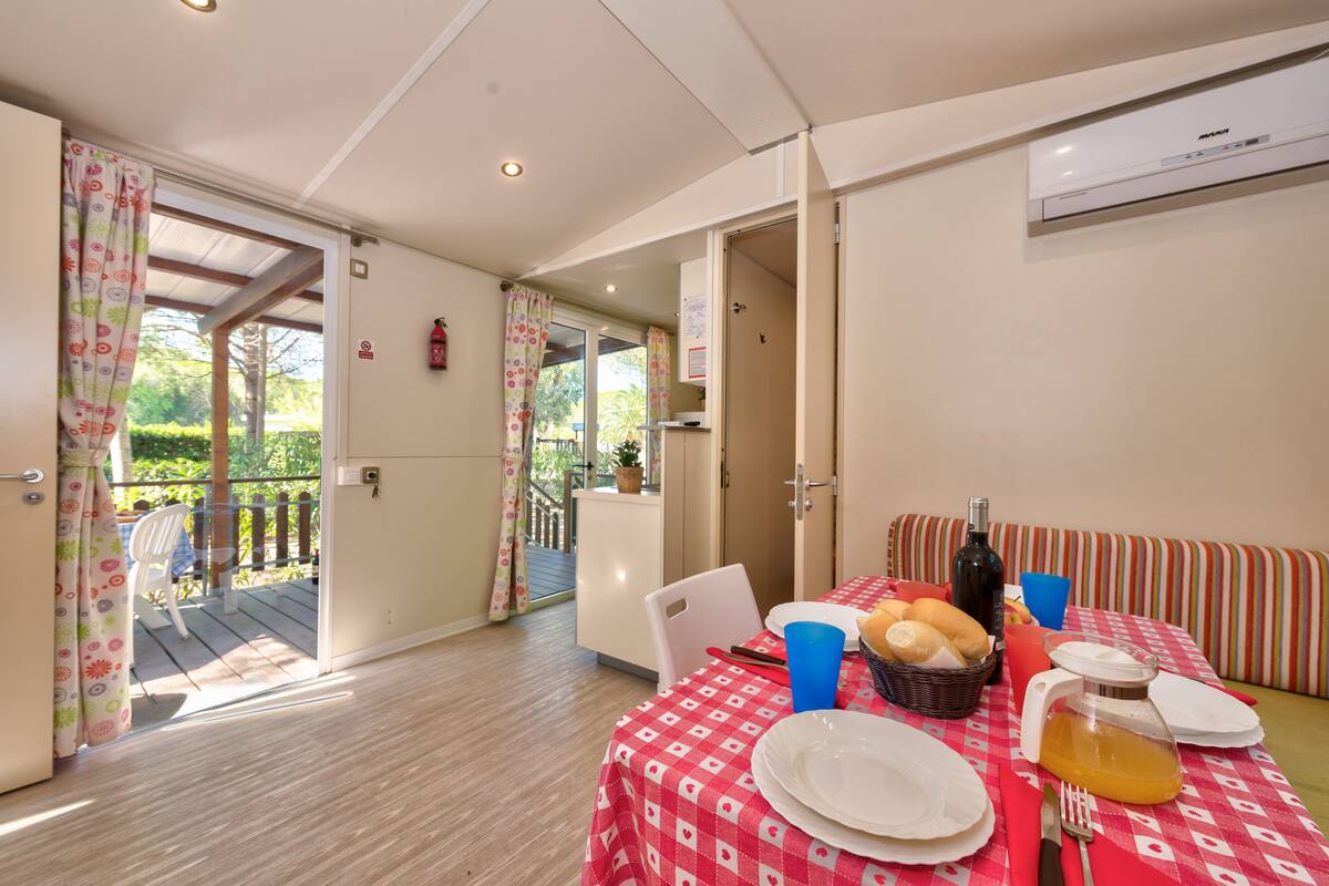 A dining area with a table set for two, a wicker basket with bread, a bottle, and a pitcher of juice.