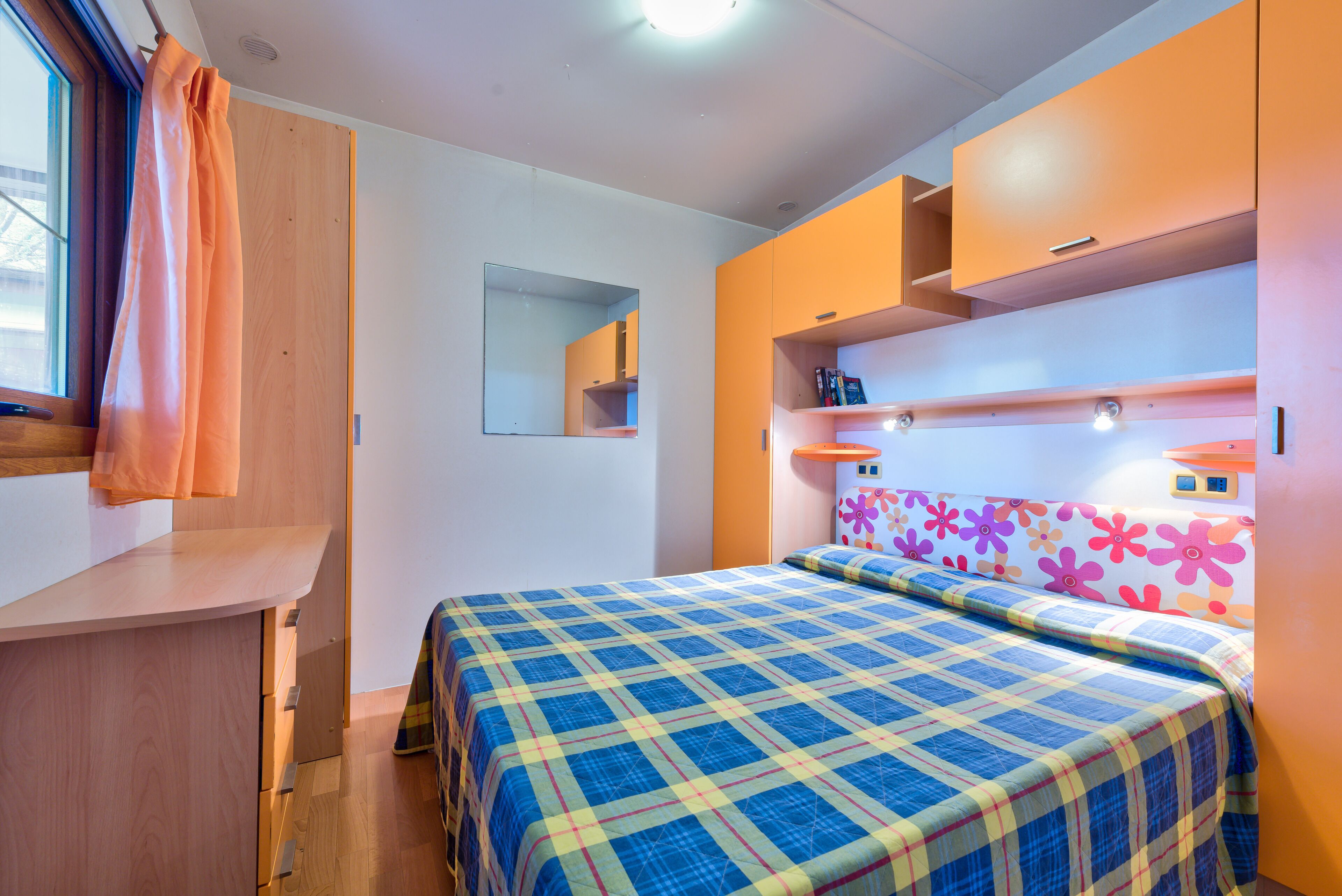Un dormitorio con cama, armario, espejo y ventana con cortinas.