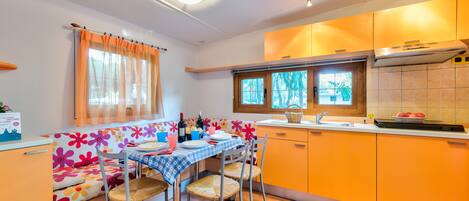 A compact kitchen with a dining area, featuring a table set for four, a window with curtains, and orange cabinetry.