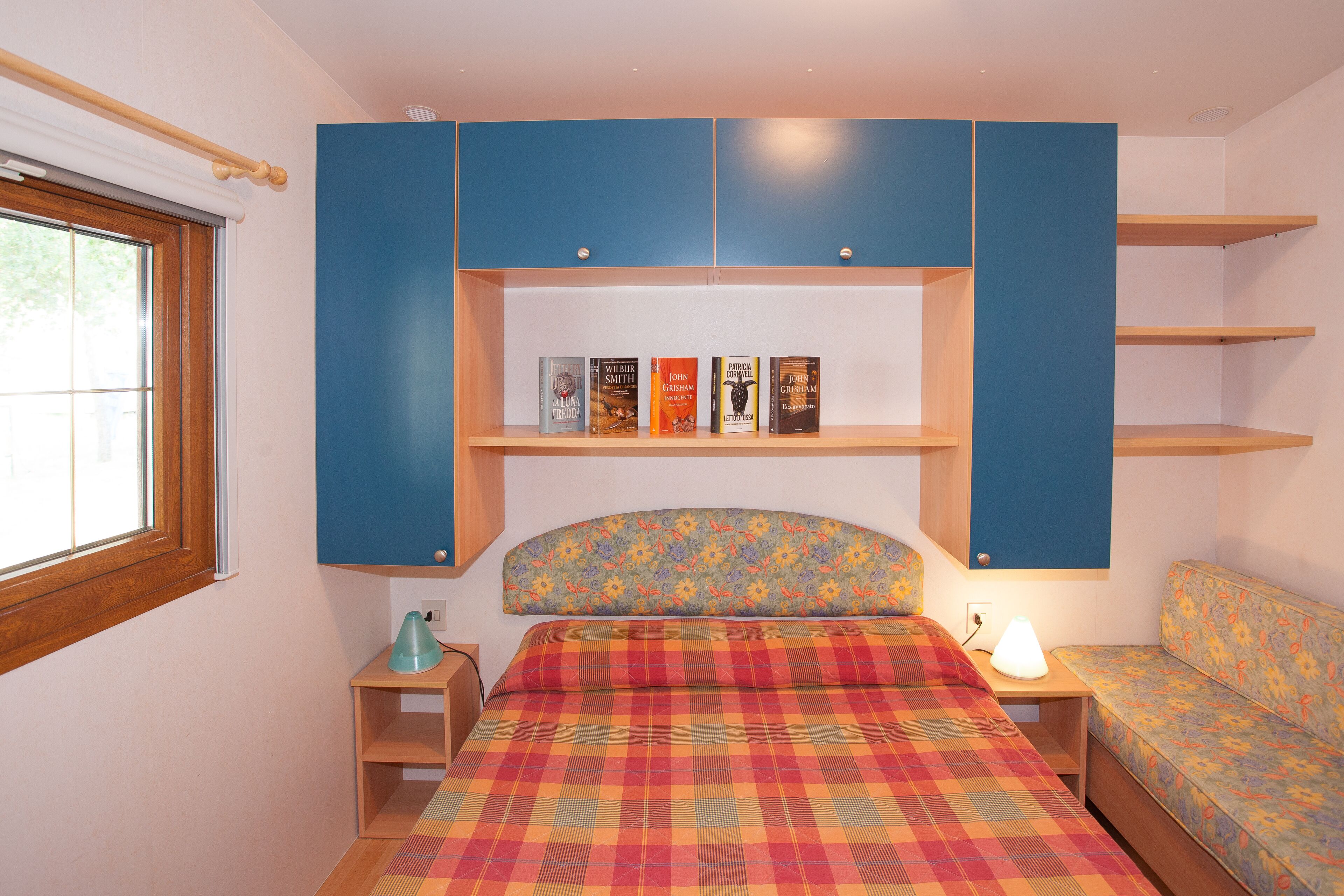 Una camera da letto con un letto, un comodino, una scrivania, un divano e mensole a muro piene di libri.