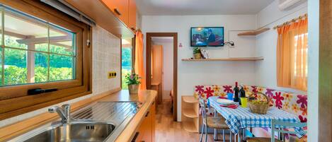 A compact kitchen with a sink, wooden cabinets, and a window overlooking greenery.