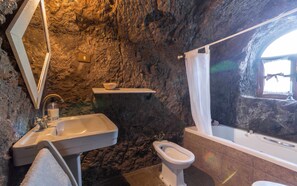 A bathroom with a stone wall, a sink, a toilet, and a bathtub. - Las Margaritas Cave House (Artenara)