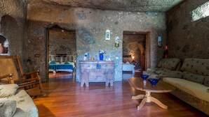 A rustic room with a stone wall, a wooden bed, a wooden table, a sofa, and a small table with bowls. - Las Margaritas Cave House (Artenara)