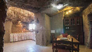 A rustic stone interior with a dining table set for two, a wooden cabinet, and a tiled floor. - Las Margaritas Cave House (Artenara)