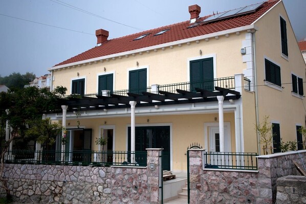 A two-story building with a stone facade, green shutters, and a red-tiled roof.