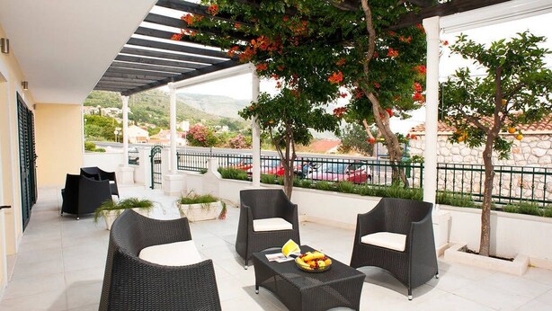 An outdoor patio with wicker furniture, a table with fruit, and a view of the street and greenery. - Vila Morska Sirena (Zupa dubrovacka)