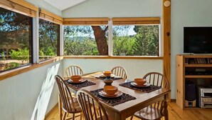 A dining area with a table set for four, surrounded by windows with a view of trees and a building.