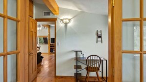 A hallway with wooden flooring, a desk with a chair, a wall-mounted ladder, and a ceiling fan.