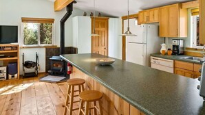 A kitchen with wooden cabinets, a central island with stools, a stove, and a large window.