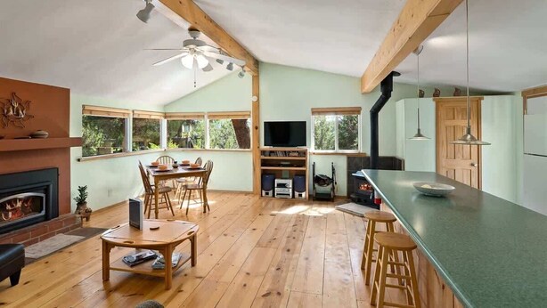 A spacious living area with a fireplace, wooden flooring, a dining table, and a kitchen with a large island.