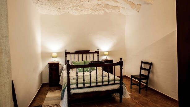 Een slaapkamer met een houten bed, twee nachtkastjes met lampen, een stoel en een gestructureerd plafond.