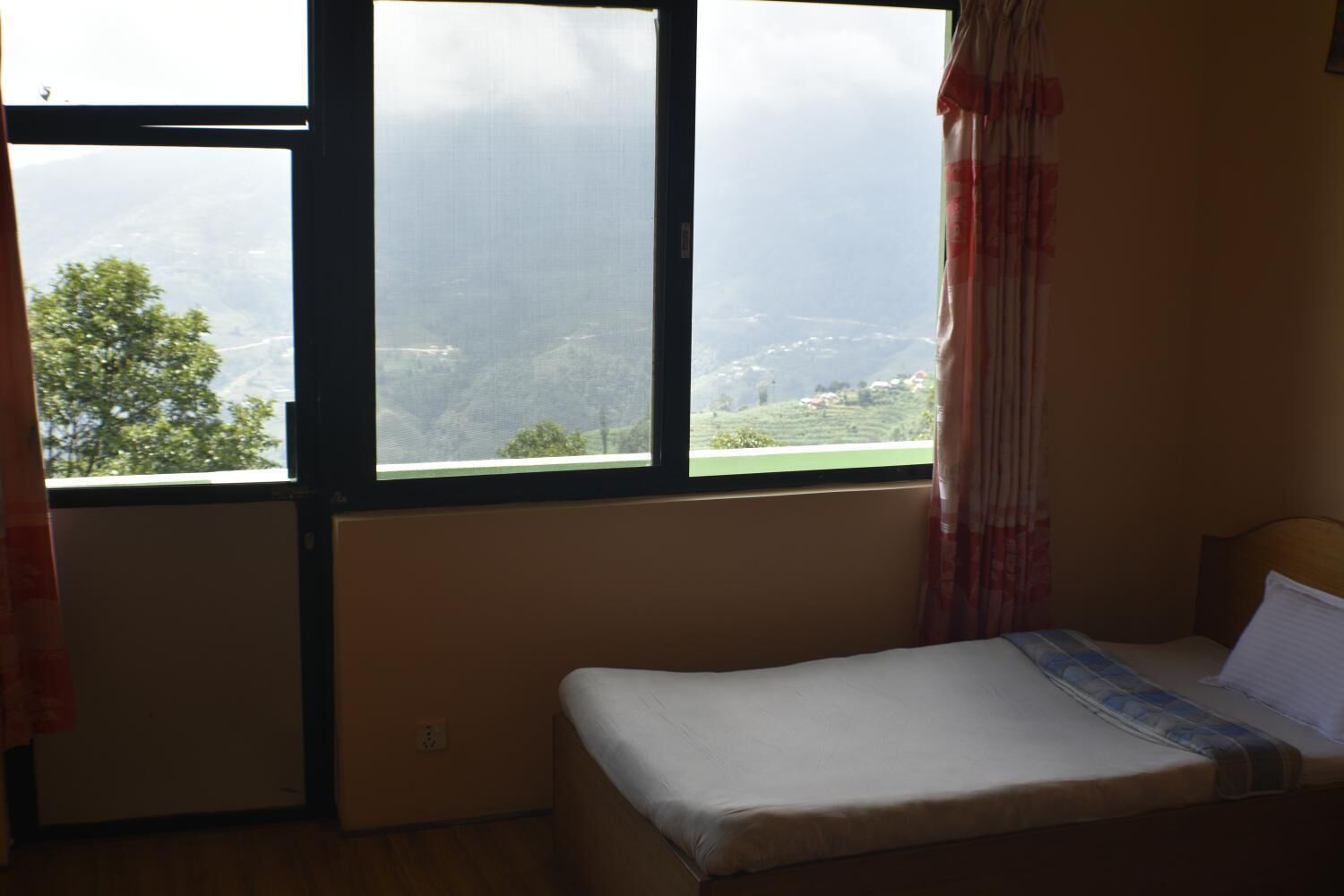 A room with a bed, a window with a view of a green landscape, and a curtain.
