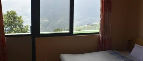 A room with a bed, a window with a view of a green landscape, and a curtain.