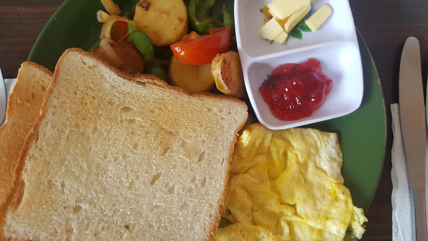 A plate with toast, scrambled eggs, roasted potatoes, and a side of jam.