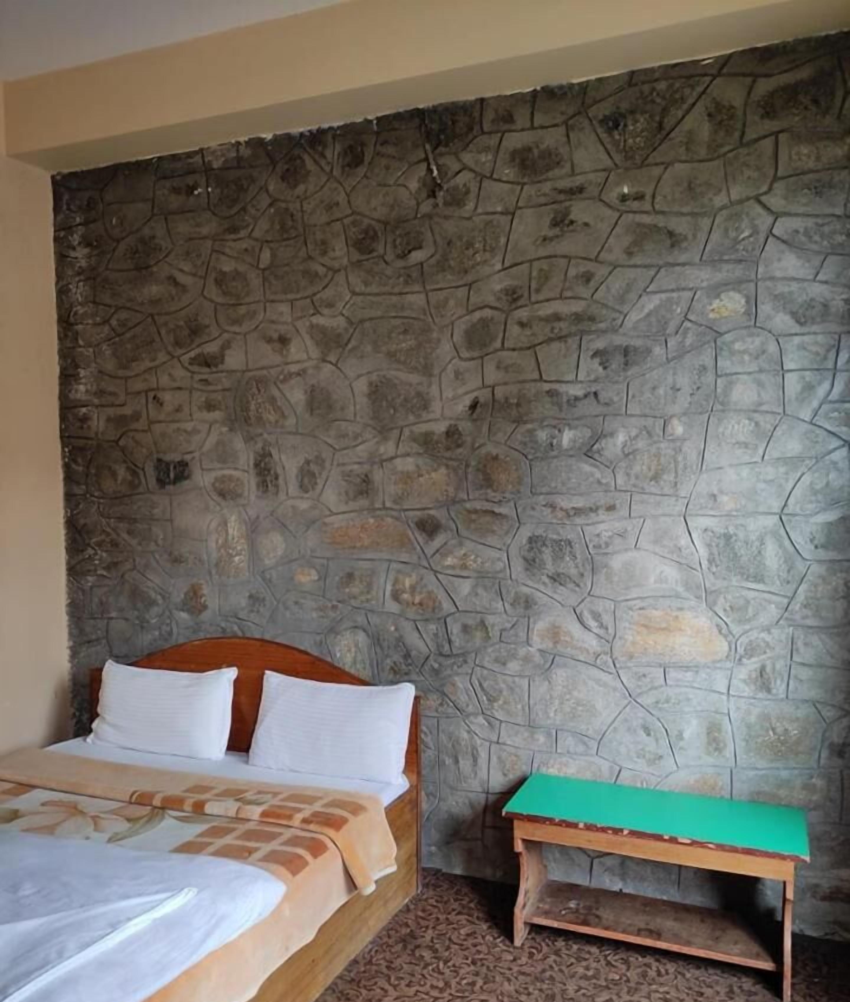 Een kamer met een stenen muur, een bed met witte beddengoed en een klein houten tafeltje met een groene blad.
