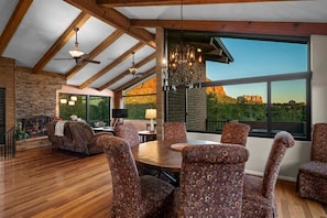 Uma sala de estar espaçosa com lareira, um espaço de refeições com cadeiras estampadas e uma grande janela com vista para uma paisagem montanhosa.