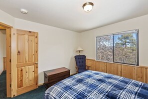 Een slaapkamer met een bed, een houten garderobe, een stoel, een raam met uitzicht en een lamp.