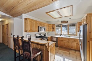 A kitchen with wooden cabinets, a central island with chairs, a microwave, stove, and a refrigerator.