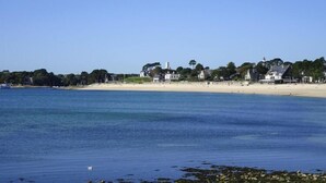 Ein Küstenblick mit einem Sandstrand, einer Häuserreihe und einem Leuchtturm in der Ferne.