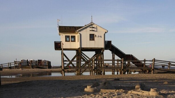 A wooden pier with a small building on stilts, a sandy beach, and a calm water body. - Reihenhaus, St. Peter - Ording (St. Peter-Ording)