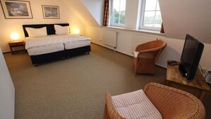 A bedroom with a bed, two bedside lamps, a television on a wooden table, and a window with curtains. - Reihenhaus, St. Peter - Ording (St. Peter-Ording)