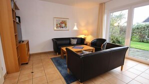 A living room with a black sofa, a wooden coffee table, and a lamp. There is a bookshelf and a painting on the wall. - Reihenhaus, St. Peter - Ording (St. Peter-Ording)