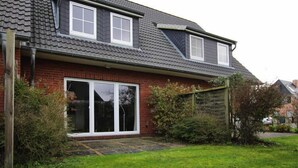 A two-story house with a sloped roof, a large sliding glass door, and a brick exterior. - Reihenhaus, St. Peter - Ording (St. Peter-Ording)