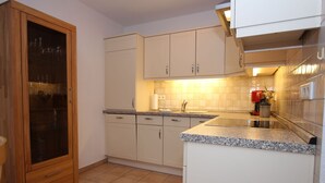 A kitchen with light-colored cabinets, a granite countertop, and a tiled backsplash. - Reihenhaus, St. Peter - Ording (St. Peter-Ording)