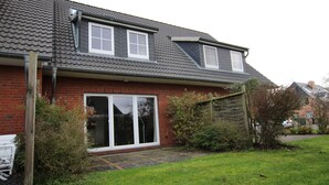 A two-story house with a red brick exterior, large sliding glass doors, and a sloped roof. - Reihenhaus, St. Peter - Ording (St. Peter-Ording)