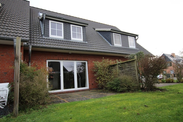 A two-story house with a red brick exterior, large sliding glass doors, and a sloped roof.