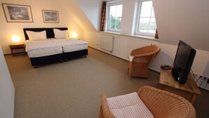 A bedroom with a bed, two bedside lamps, a television on a wooden stand, and a window with curtains. - Reihenhaus, St. Peter - Ording (St. Peter-Ording)