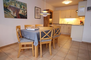 A dining area with a table set for four, wooden chairs, a blue tablecloth, and a painting on the wall.