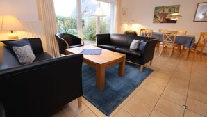 A living room with a sofa, coffee table, and dining area with chairs and a table. - Reihenhaus, St. Peter - Ording (St. Peter-Ording)